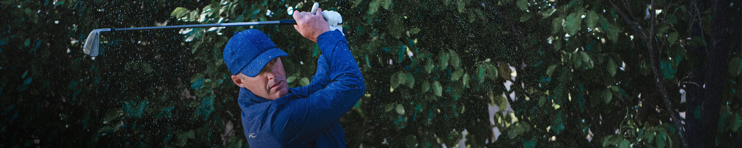 A man wearing a KJUS Pro 3L 3.0 Jacket swings a wedge in the rain.